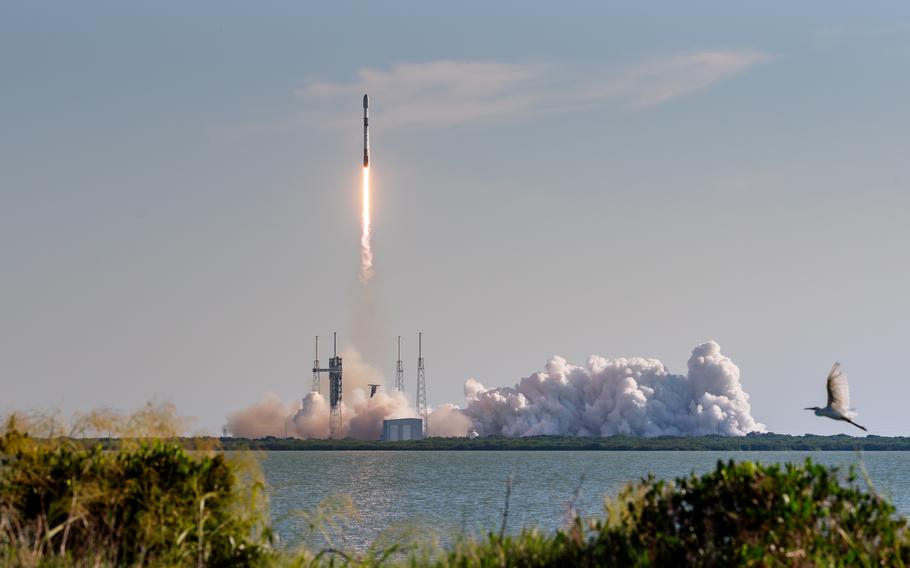 A rocket blasts off from a launch pad near the water.