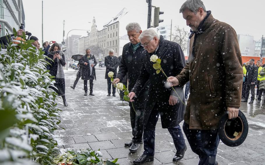 Three men bend forward slightly to place white roses on an impromptu memorial arrangement.