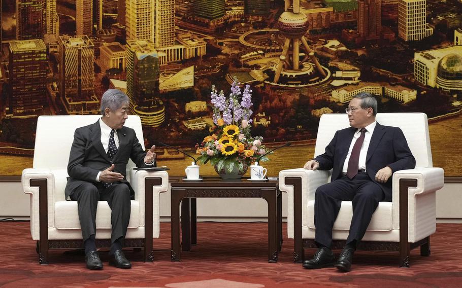 Japan’s Foreign Minister Takeshi Iwaya and Chinese Premier Li Qiang sit in white arm chairs facing the audience.