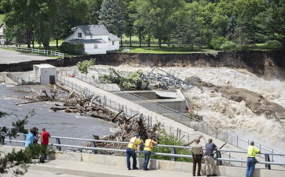 Onlookers take in the catastrophic damage to the Rapidan Dam site in Rapidan, Minn., Monday, June 24, 2024. Debris blocked the dam forcing the heavily backed up waters of the Blue Earth River to reroute along the bank nearest the Dam Store. (Casey Ek/The Free Press via AP)