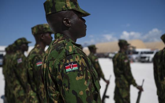 A police officer in camouflage in-focus in the foreground with other officers seen out-of-focus lined up next to him.