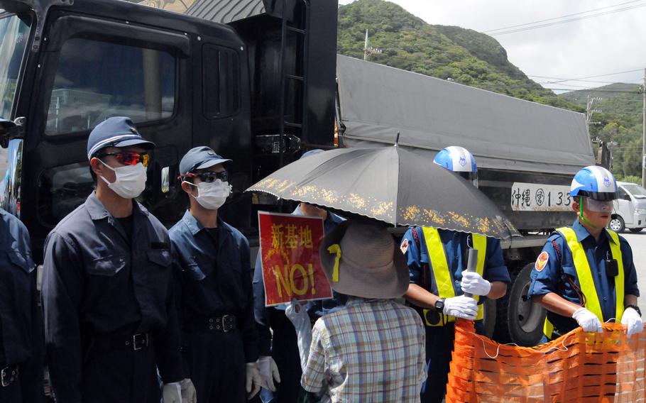 More than 40 security guards and police officials block protesters at the entrance to Awa port in Nago city, Okinawa, Thursday, Aug. 22, 2024. 