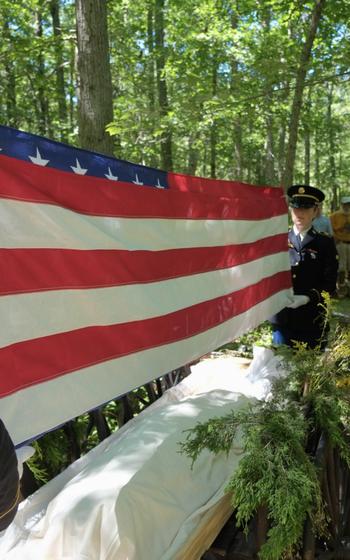 A folded American flag is held over a shroud covering the body of WWII veteran Edward Hoffner.