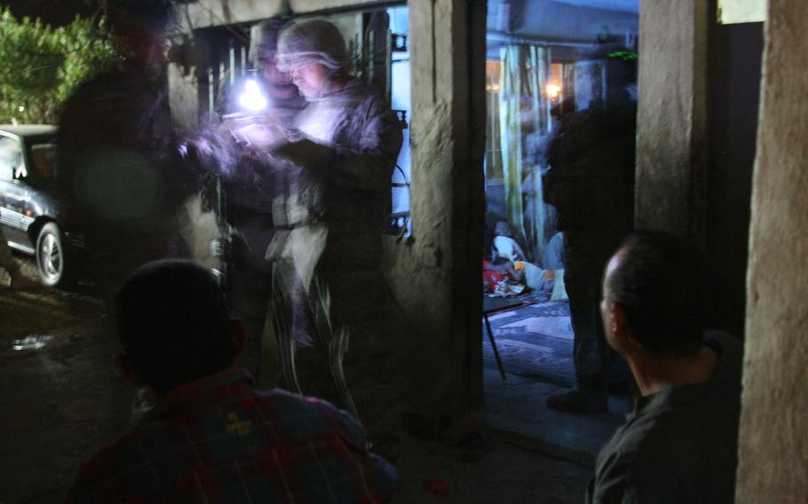 Two temporarily detained Iraqi men, foreground,  watch as U.S. troops with Company A, 1-30th Infantry, 2nd Brigade, 3rd Infantry Division search the home of a man suspected of helping insurgents direct mortar fire at Forward Operating Base Murray in Iraq’s Arab Jabour district on the southeast of Baghdad. U.S. troops with Task Force Marne launched a massive sweep to halt the flow of insurgents and weapons into the Iraqi capital.