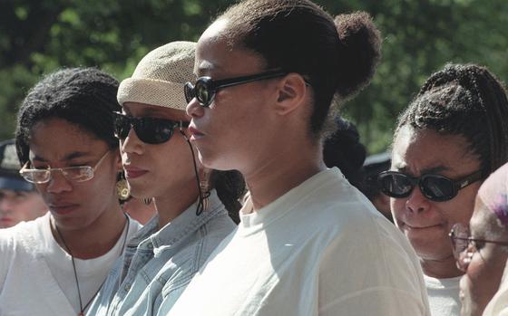 Four women in sunglasses stand outside while they speak with reporters.