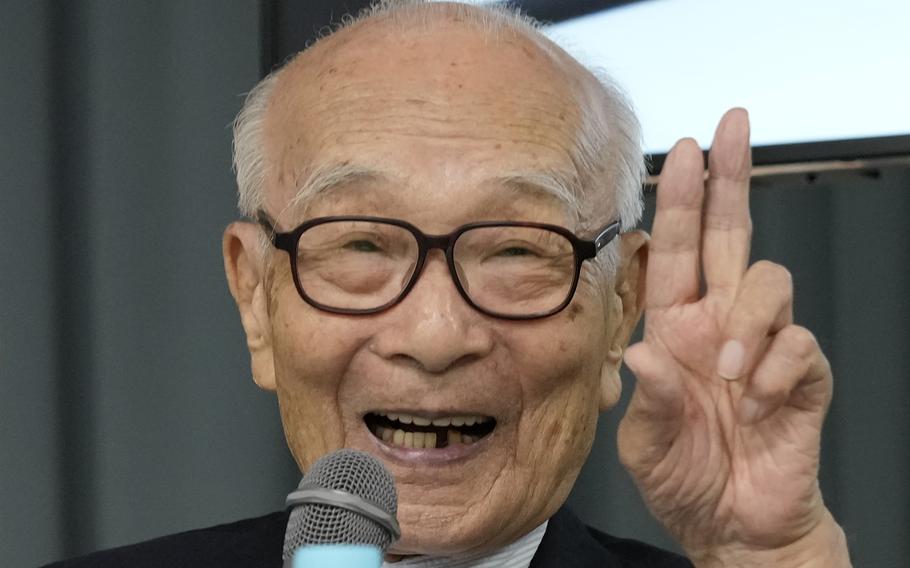 An older Japanese man speaks in front of a microphone.