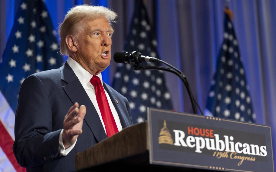 Donald Trump speaks into a microphone while standing at a podium in front of U.S. flags.