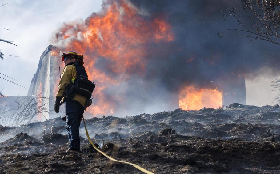 A firefighter turns away from the heat of a fully engulfed home while battling the Edgehill fire on August 5, 2024 in San Bernardino, Calif.