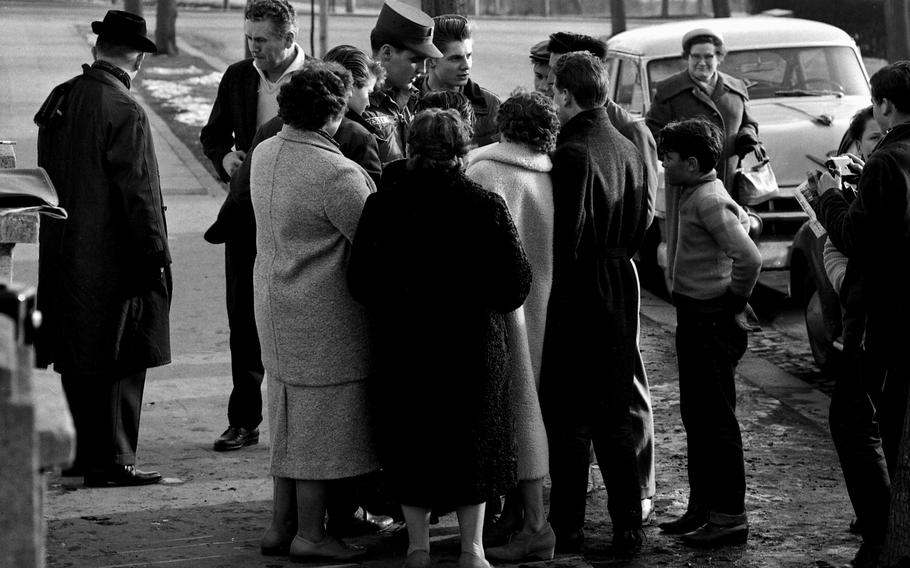 Elvis Presley stands in uniform, surrounded by fans, during his time in the Army.