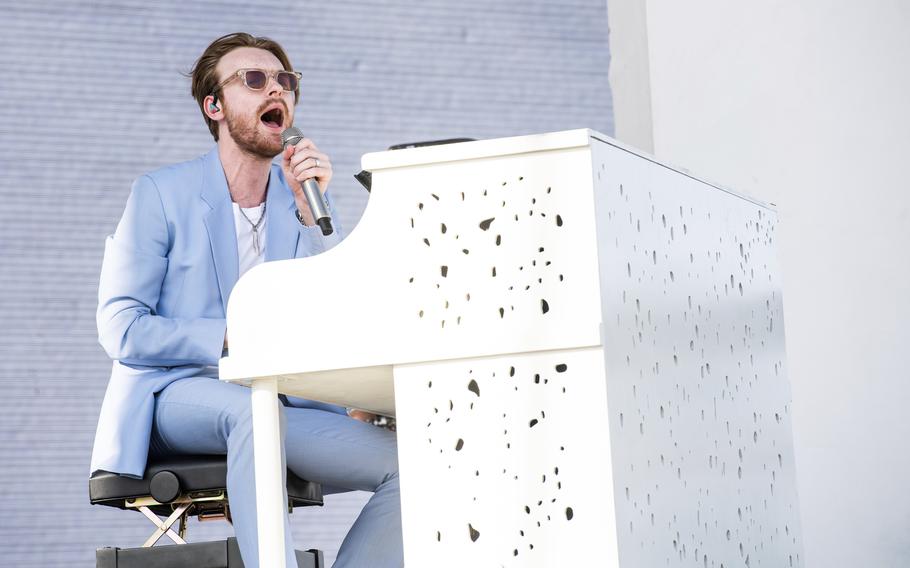 Musical artist and producer FINNEAS sits and sings at a white piano.