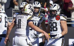 Navy quarterback Blake Horvath raises his arms to embrace teammates to celebrate a touchdown during a college football game.