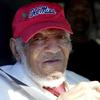 An elderly man in a red Ole Miss ball cap smiles slightly from his seat inside a car.