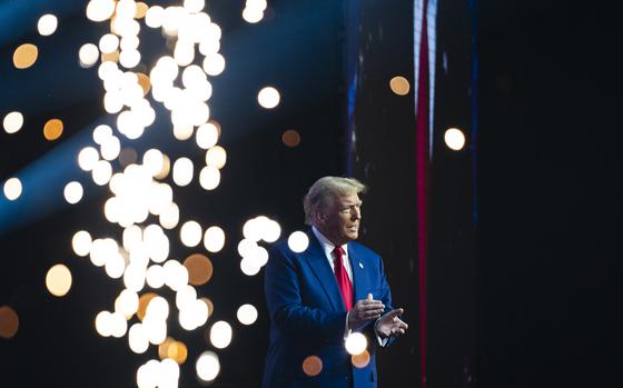 Donald Trump claps while standing in front of lights.