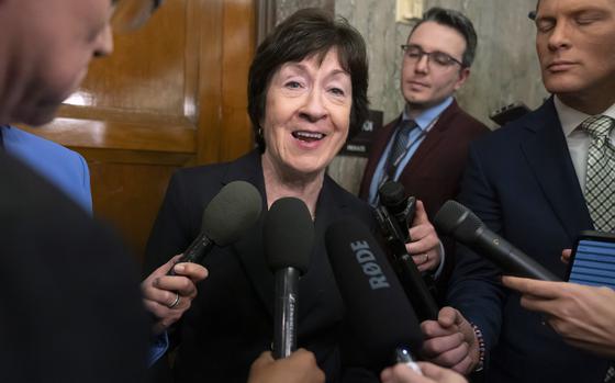 Sen. Susan Collins is surrounded by reporters holding microphones as she speaks in a hallway at the U.S. Capitol.