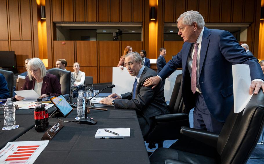 Graham pats a seated Merkley on his shoulder as he moves his chair to sit down during the hearing.