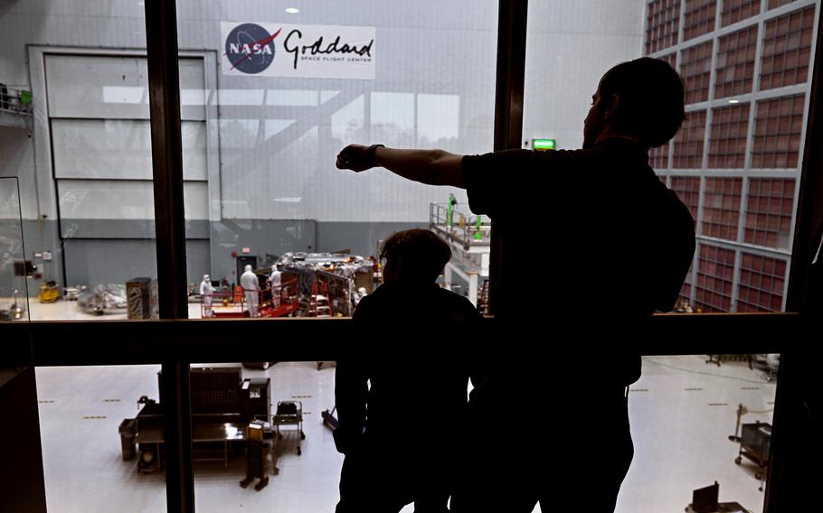 Two people, in shadow, look through the window into the room where the telescope is being assembled.