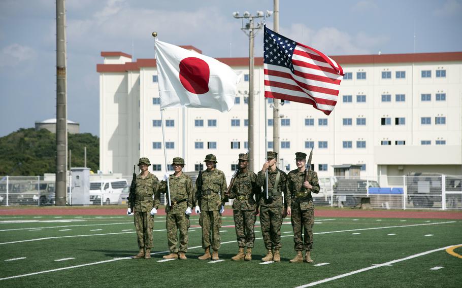 U.S. Marines and Japanese soldiers display their flags on a green field.