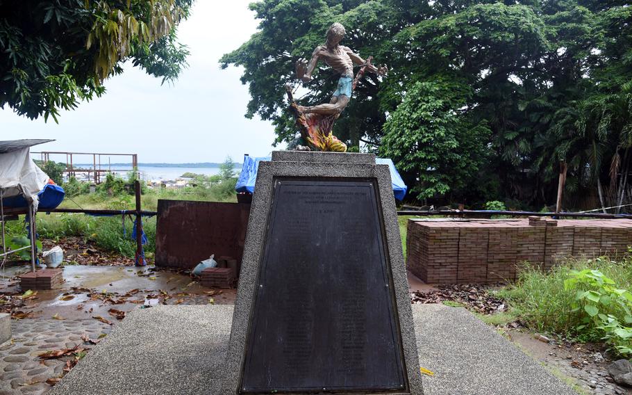 A stone memorial is topped with a statue of an emaciated man.