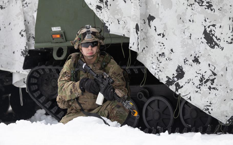 A soldier with the Alaska-based 11th Airborne Division crouches near a military vehicle.