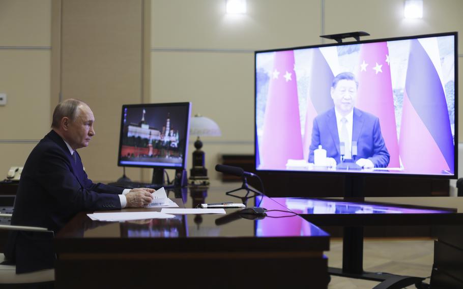 Putin sits at a desk to talk with Xi, who appears on a video screen.