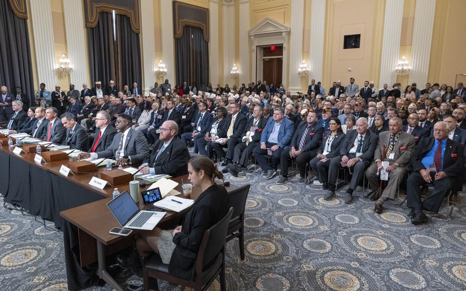 A crowd of people sit in rows of chairs behind a table of others testifying in a congressional hearing room.