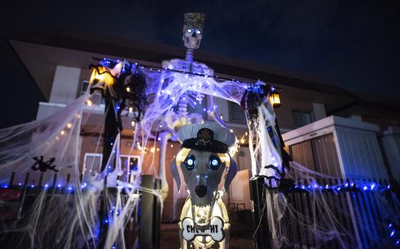 A large, illuminated skeleton Halloween decoration stands outside a house at night.