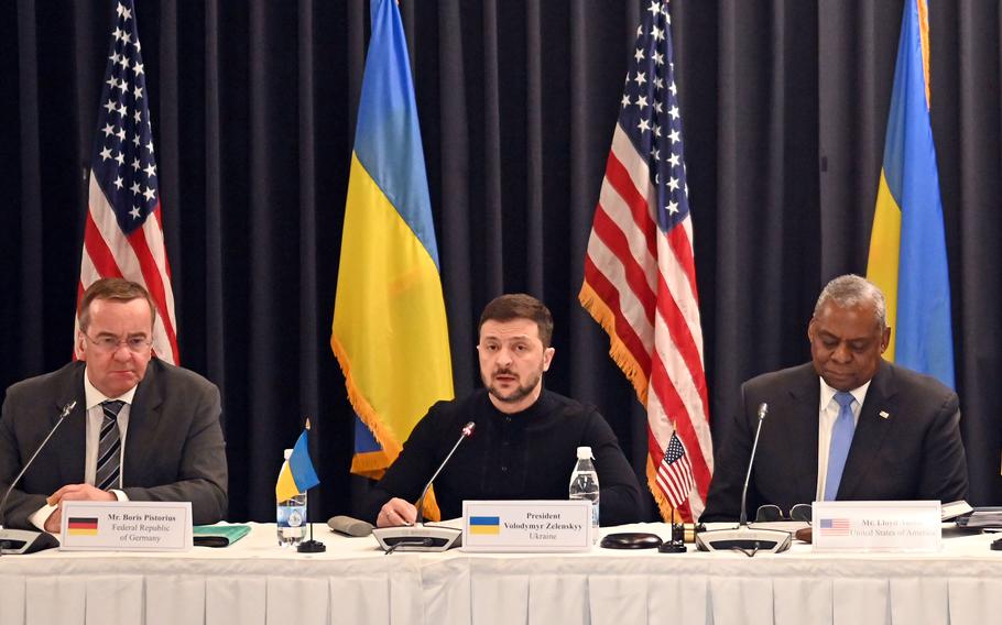 Ukrainian President Volodymyr Zelenskyy sits at a white table while speaking into a microphone.