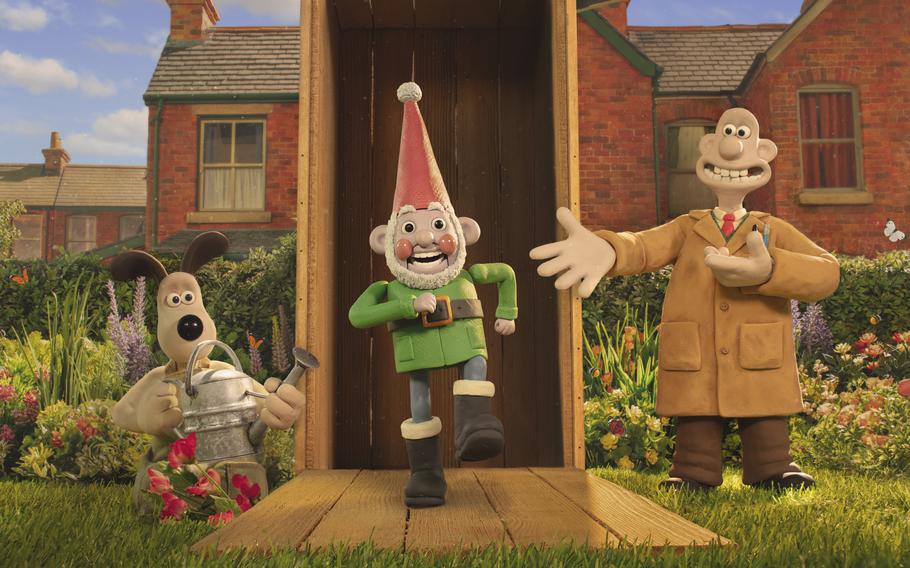 A stop-motion animation dog carrying a water can, a stop-motion animation gnome and a stop-motion animation human in front of a house in a garden.