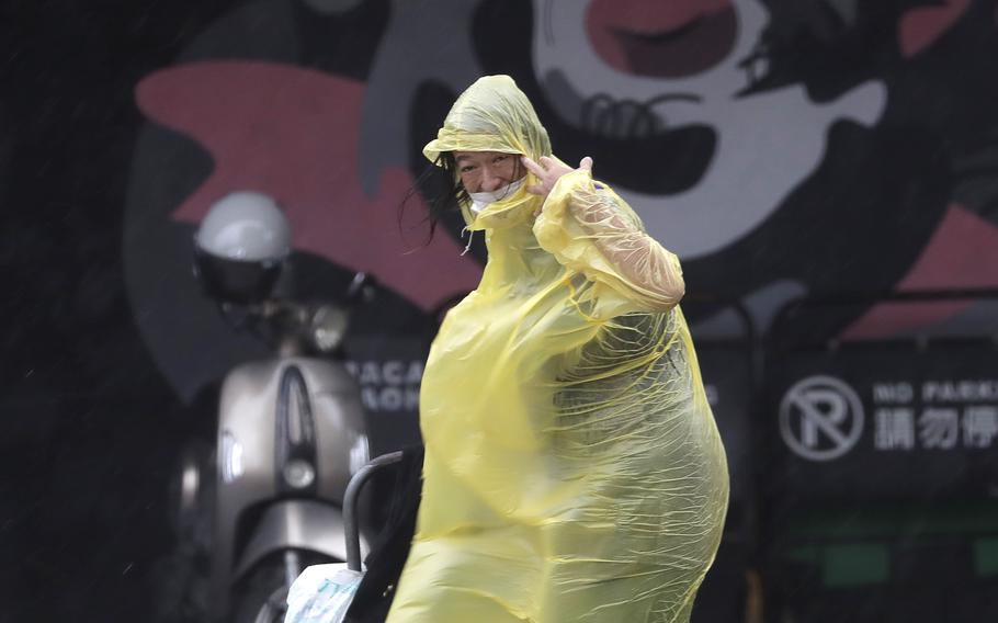 A woman wearing a yellow poncho walks through rain and wind from Typhoon Krathon.