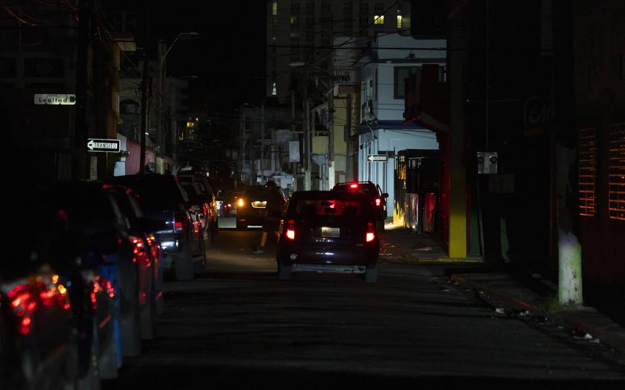 A street is dark in San Juan, with only the tail lights of cars to illuminate the scene.