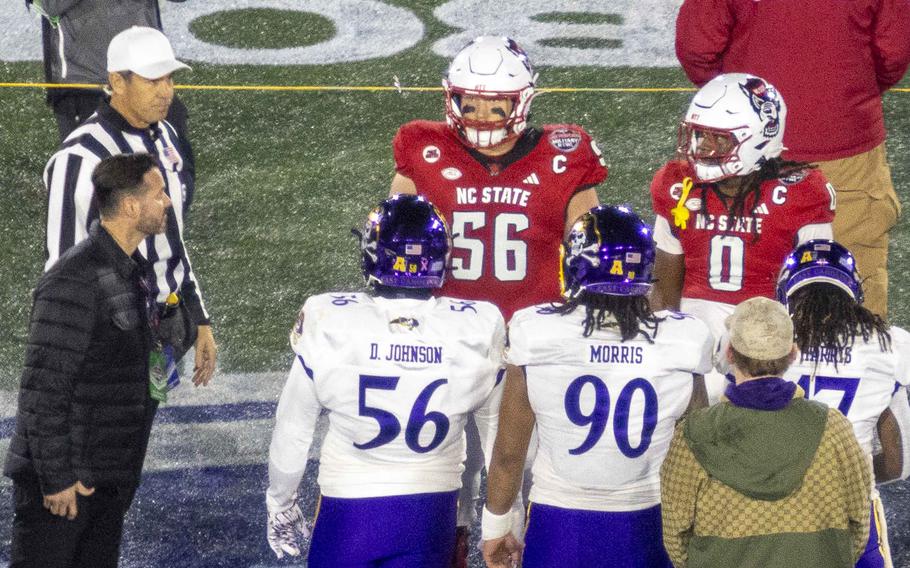 Football players on opposing teams face each other on the sidelines.