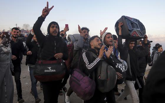 Displaced Palestinians carrying bags clap and hold up peace signs as they walk along a road into the northern Gaza Strip.