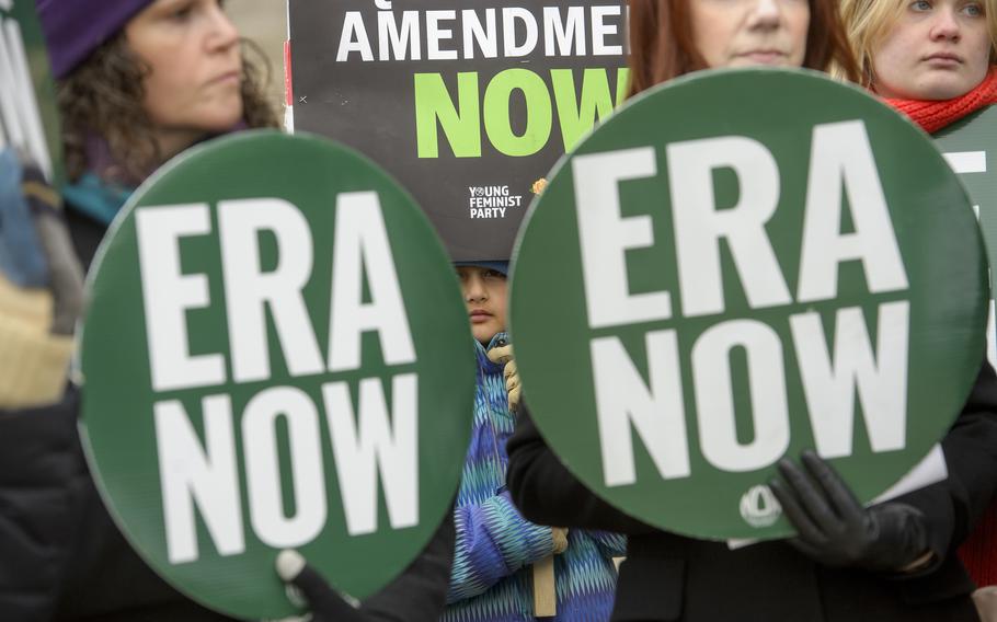 A girl is seen in between “ERA NOW” signs as people hold a rally.