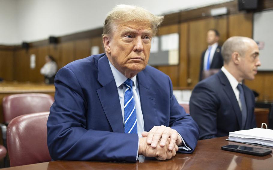 Donald Trump sits at a table in a courtroom with his hands folded in front of him.