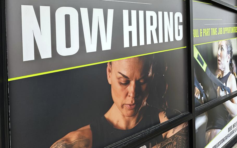 Bold, capitalized text reading ‘Now hiring’ hovers over an image of a person exercising, on a poster for a fitness center.