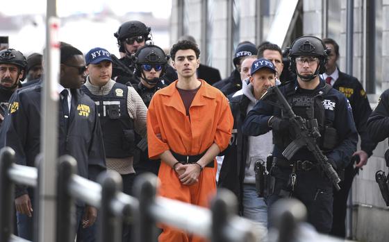 Luigi Mangione in an orange jumpsuit in the center of the photo, with numerous police officers surrounding him.