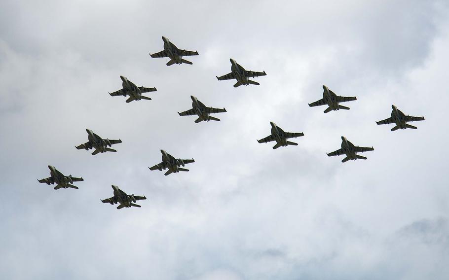 A group of 12 military fighter jets, seen from below, fly in formation.