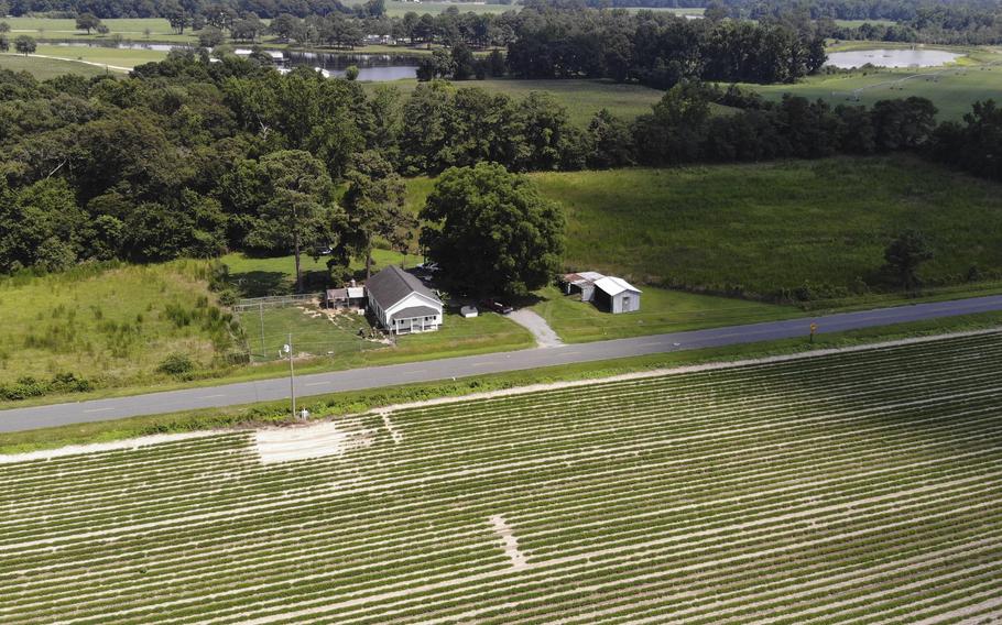 Green fields and trees surround a white farmhouse.