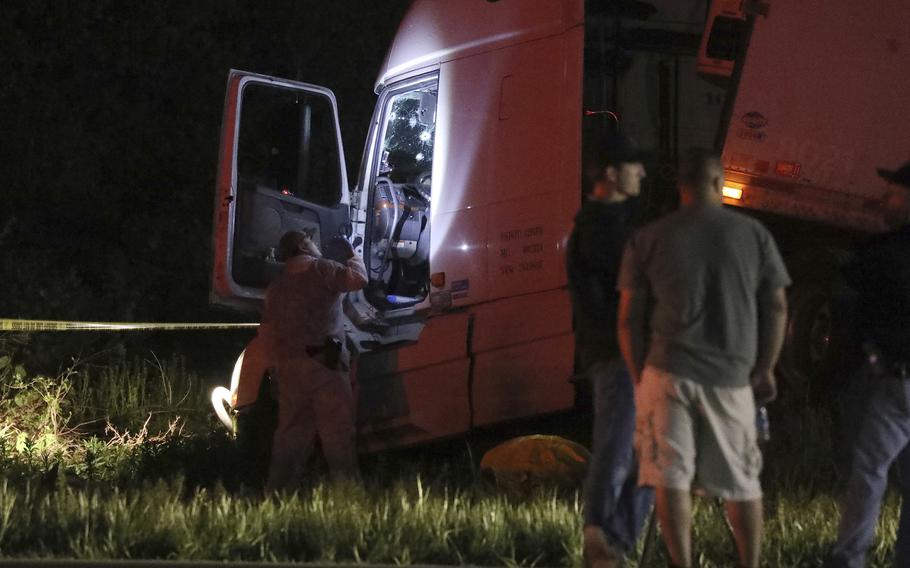 An investigator shines a flashlight into the cab of a tractor trailer in the dark. 