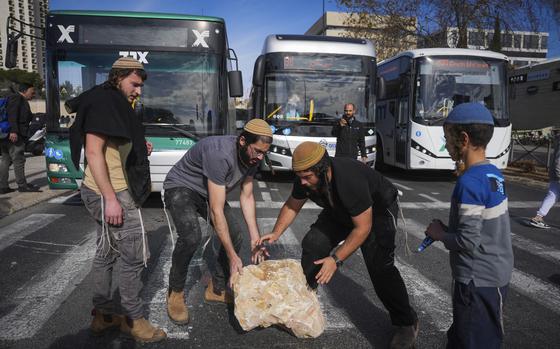 Israeli activists move a large stone meant to block a road in protest of the seemingly imminent ceasefire deal with Hamas.