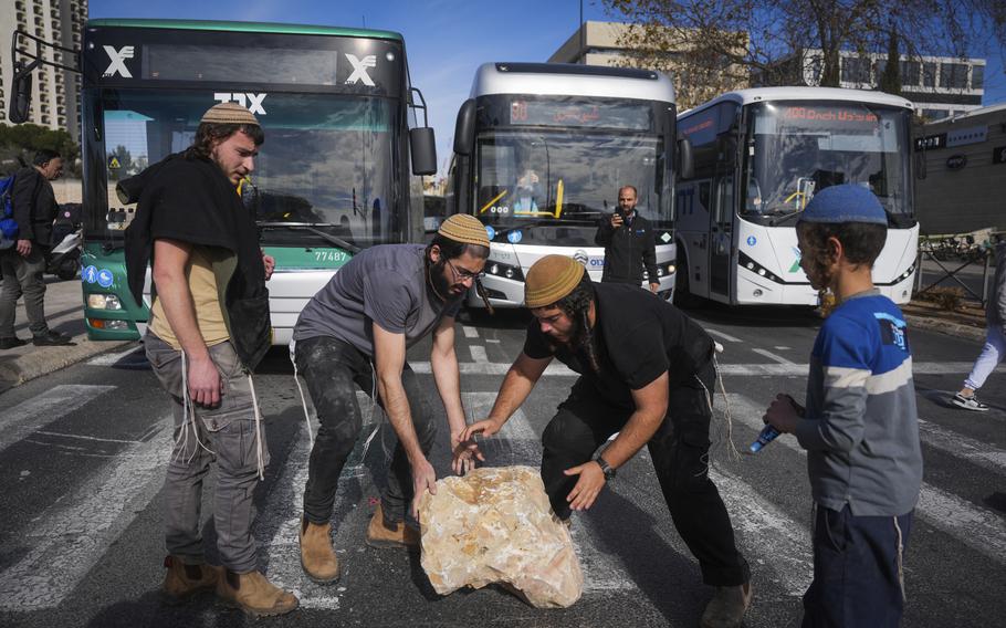 Israeli activists move a large stone meant to block a road in protest of the seemingly imminent ceasefire deal with Hamas.