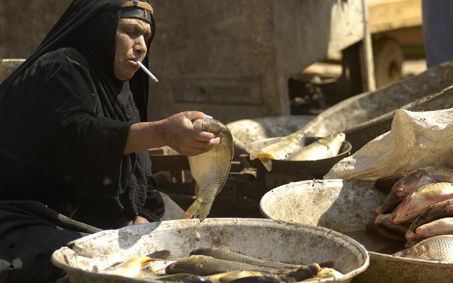 An Iraqi woman shuffles fish from a basin for passersby to purchase in Oubaidy’s market.