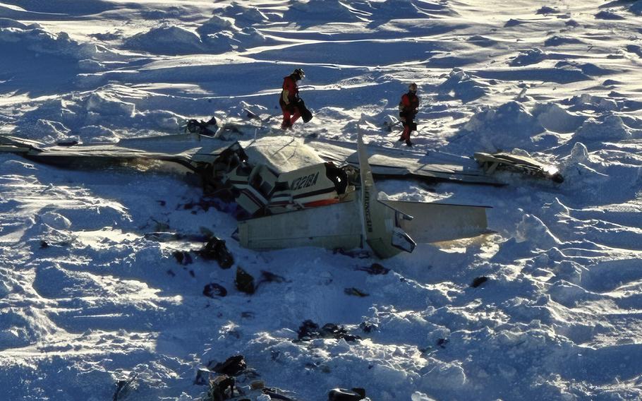 Two people walk around a small commuter plane that crashed in the snow.