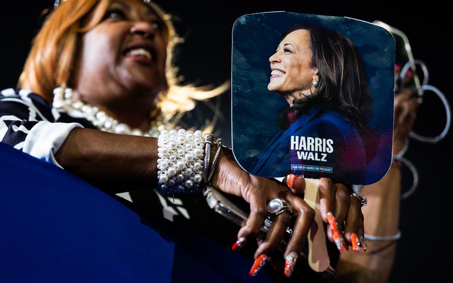 A woman holds a fan with a picture of Kamala Harris on it.