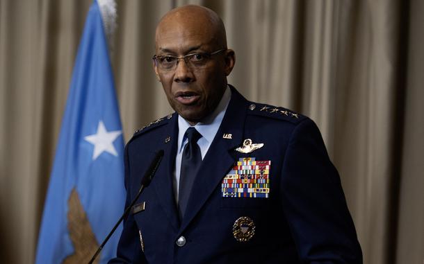 An Air Force officer in blue dress uniform stands at a podium and speaks into a microphone.