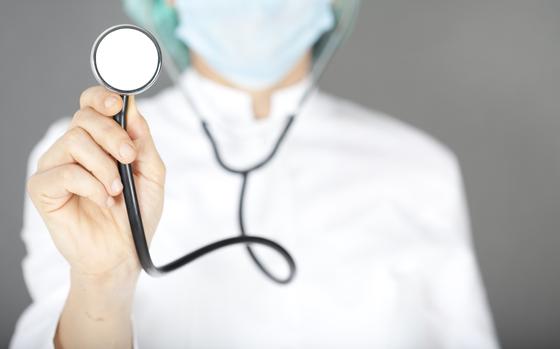 Doctor holding stethoscope on grey background