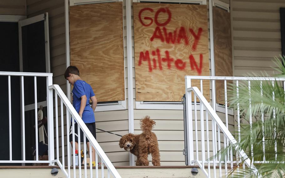 A boy walks a dog on a leash in front of a boarded up window that reads, go away Milton.