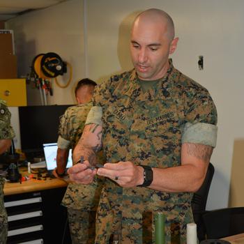 Marine Corps Gunnery Sgt. Mark Cureo displays a polymer camera mount used on a drone that was manufactured using a 3D printer as part of an experimental phase during the Rim of the Pacific exercise at Marine Corps Base Hawaii on July 2, 2024.