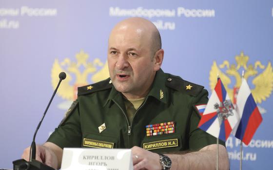 A man in a military uniform sits and speaks in front of a microphone.