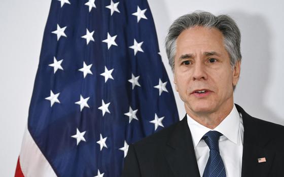 A man with gray hair and wearing a suit and blue tie speaks in front of an American flag.